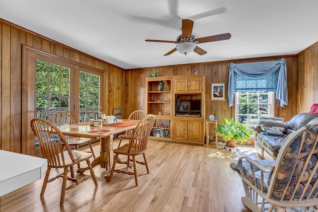 dining area with light wood-type flooring, crown molding, ceiling fan, and wood walls