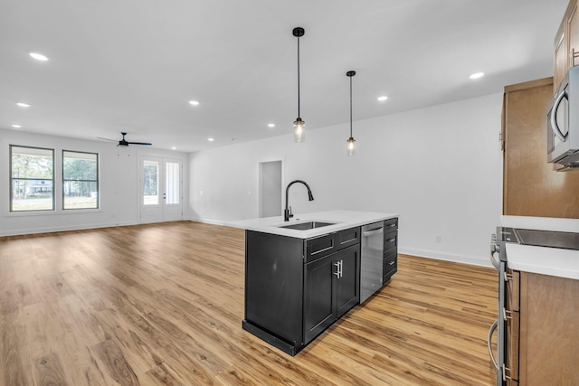 kitchen with sink, a center island with sink, appliances with stainless steel finishes, pendant lighting, and light hardwood / wood-style floors