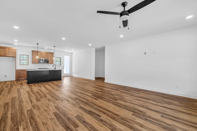 unfurnished living room with wood-type flooring, sink, and ceiling fan