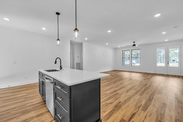 kitchen featuring decorative light fixtures, a center island with sink, sink, and light hardwood / wood-style flooring