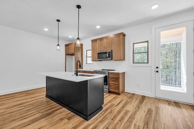 kitchen featuring pendant lighting, sink, stainless steel appliances, light hardwood / wood-style floors, and an island with sink