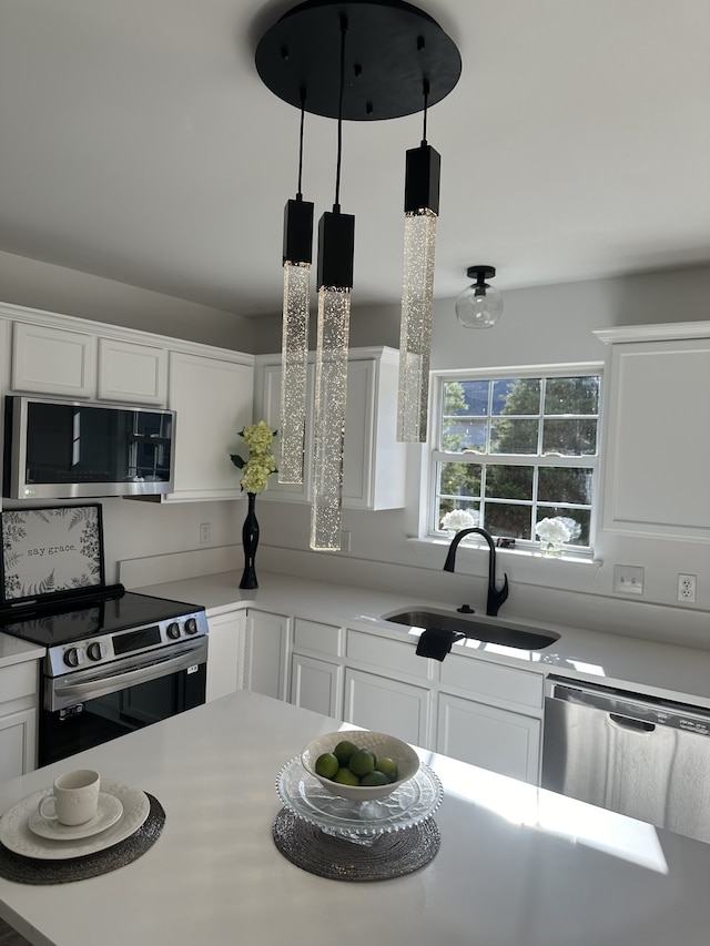 kitchen with decorative light fixtures, sink, white cabinetry, and appliances with stainless steel finishes