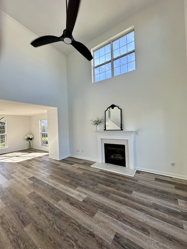 unfurnished living room with ceiling fan, dark hardwood / wood-style floors, and a high ceiling