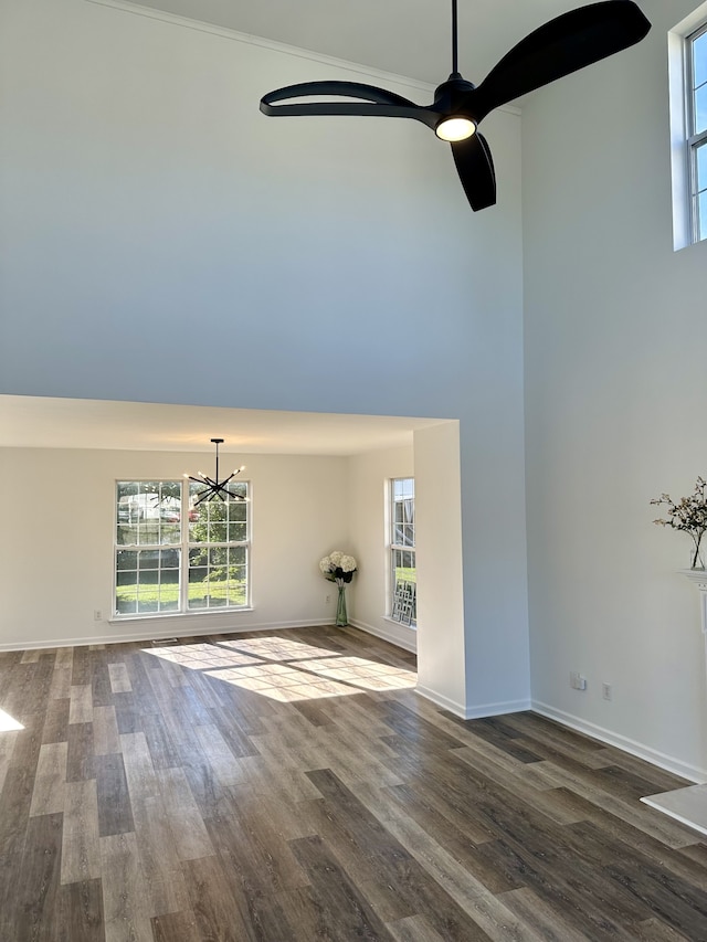 unfurnished living room featuring dark wood-type flooring, ornamental molding, and ceiling fan with notable chandelier