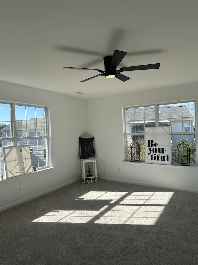 empty room featuring ceiling fan, dark carpet, and a wealth of natural light