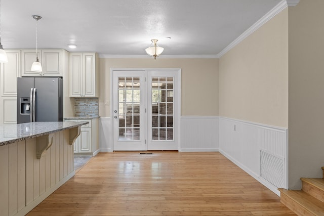 kitchen featuring light stone countertops, hanging light fixtures, light hardwood / wood-style floors, and stainless steel fridge