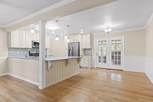 kitchen with kitchen peninsula, stainless steel appliances, a breakfast bar, pendant lighting, and light wood-type flooring