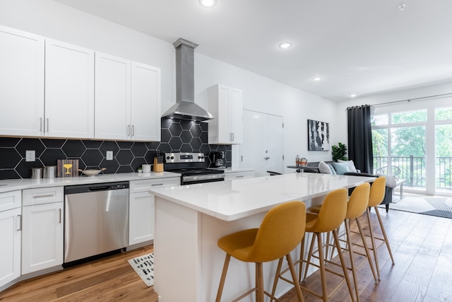 kitchen featuring wall chimney exhaust hood, light hardwood / wood-style floors, a kitchen island, stainless steel appliances, and white cabinetry