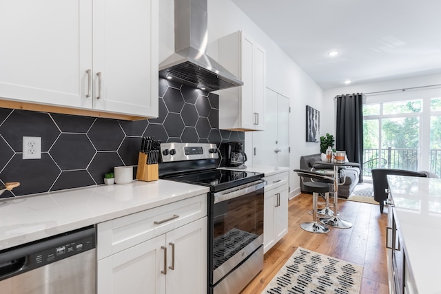 kitchen featuring appliances with stainless steel finishes, light wood-type flooring, wall chimney range hood, and white cabinets