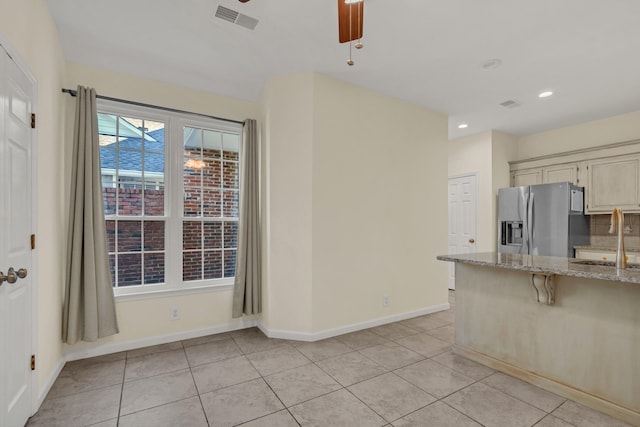 kitchen with light stone counters, baseboards, stainless steel refrigerator with ice dispenser, and a sink
