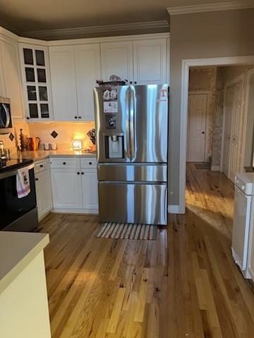 kitchen with appliances with stainless steel finishes, crown molding, white cabinetry, and light hardwood / wood-style floors