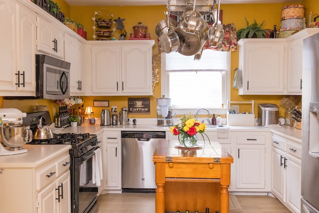 kitchen with appliances with stainless steel finishes, white cabinetry, sink, and light hardwood / wood-style flooring