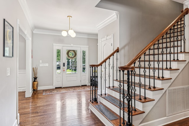 entrance foyer featuring ornamental molding, dark wood-type flooring, and a notable chandelier