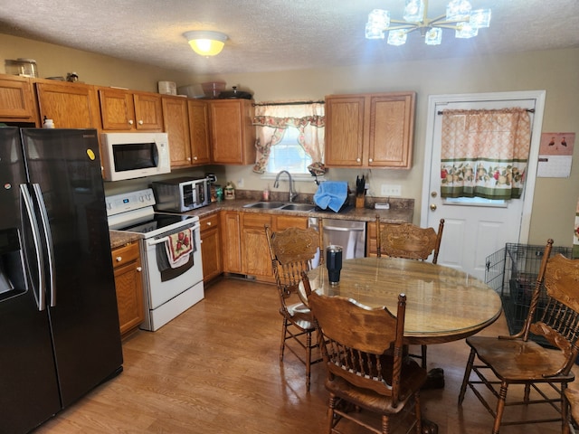 kitchen featuring sink, a textured ceiling, stainless steel appliances, light hardwood / wood-style flooring, and an inviting chandelier