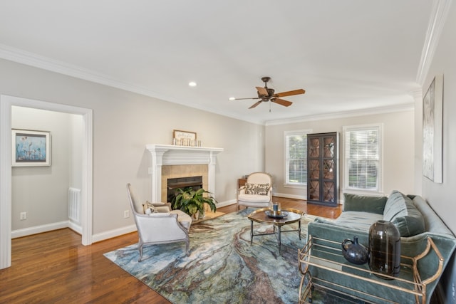 living room featuring crown molding, a tiled fireplace, wood-type flooring, and ceiling fan