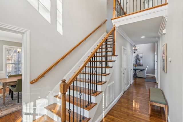 staircase featuring ornamental molding, a chandelier, wood-type flooring, and a towering ceiling