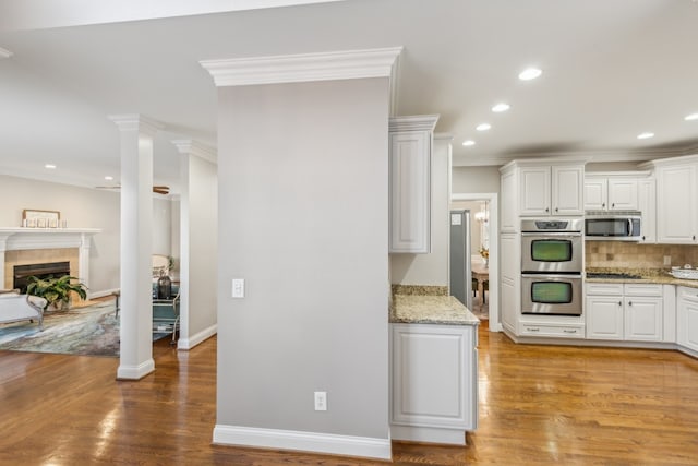 kitchen with appliances with stainless steel finishes, white cabinetry, light stone counters, ornamental molding, and light hardwood / wood-style flooring