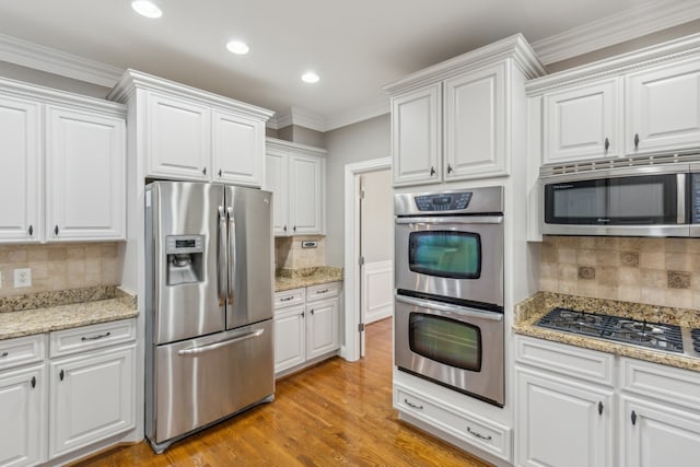 kitchen with light hardwood / wood-style floors, appliances with stainless steel finishes, decorative backsplash, and white cabinets