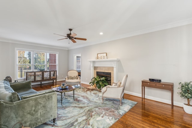 living room featuring ceiling fan, hardwood / wood-style flooring, ornamental molding, and a fireplace