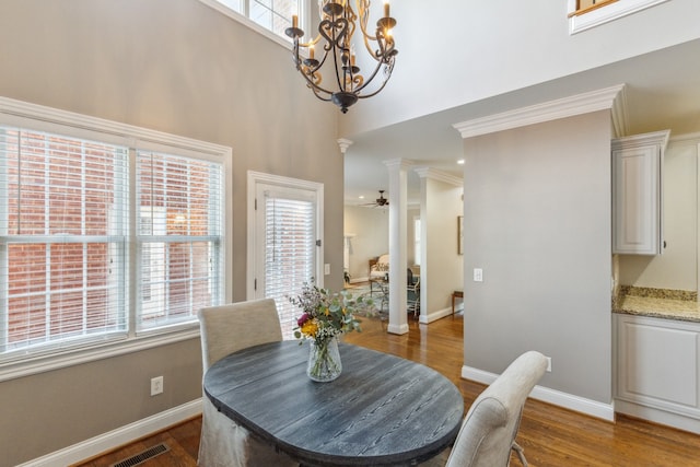 dining space featuring ceiling fan with notable chandelier, decorative columns, crown molding, a towering ceiling, and dark hardwood / wood-style flooring