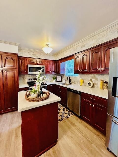 kitchen with ornamental molding, sink, a center island, light wood-type flooring, and appliances with stainless steel finishes