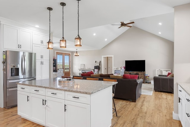 kitchen featuring light stone counters, decorative light fixtures, stainless steel fridge, a kitchen island, and white cabinets