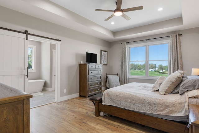 bedroom featuring multiple windows, a barn door, light wood-type flooring, and a tray ceiling