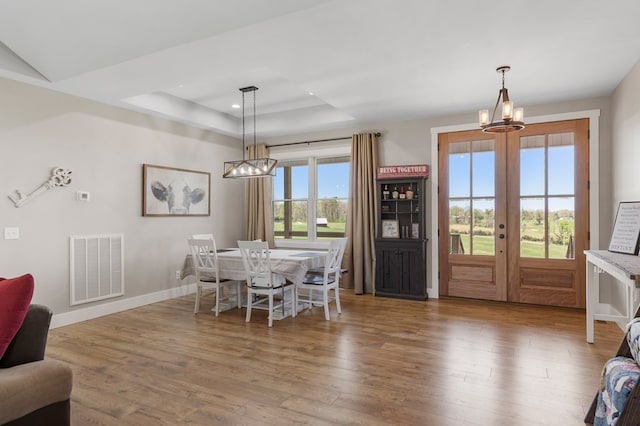 dining room with french doors, hardwood / wood-style floors, an inviting chandelier, and a tray ceiling