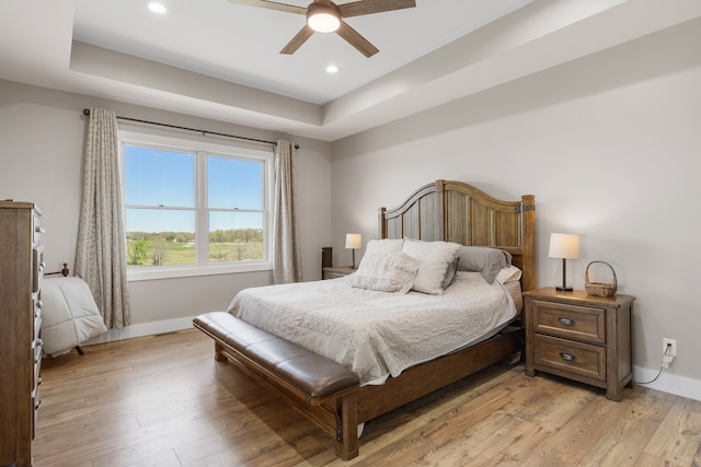 bedroom with ceiling fan, light wood-type flooring, and a tray ceiling