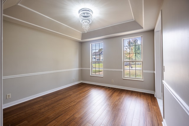 spare room with dark wood-type flooring, a raised ceiling, and a notable chandelier