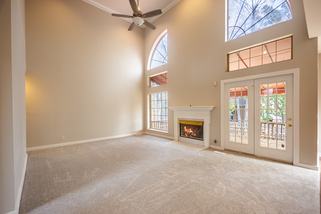 unfurnished living room with crown molding, light carpet, ceiling fan, and a towering ceiling