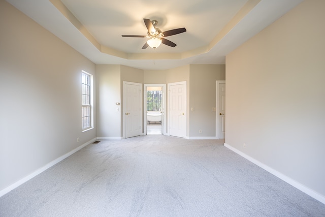 unfurnished bedroom with ensuite bathroom, ceiling fan, carpet flooring, and a raised ceiling