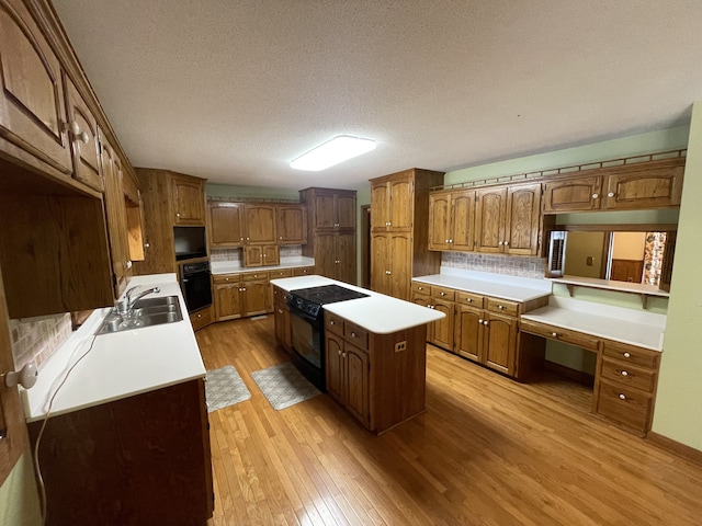 kitchen featuring sink, black appliances, a center island, a textured ceiling, and light hardwood / wood-style floors