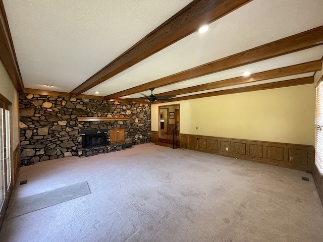 unfurnished living room featuring a wood stove, beam ceiling, carpet, and ceiling fan