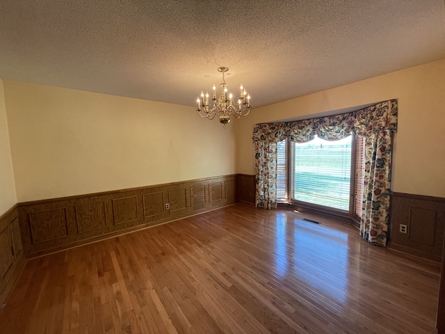 empty room featuring hardwood / wood-style floors, a textured ceiling, and an inviting chandelier