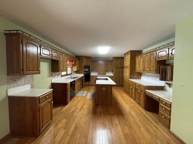 kitchen with black appliances, backsplash, a textured ceiling, a center island, and light hardwood / wood-style flooring