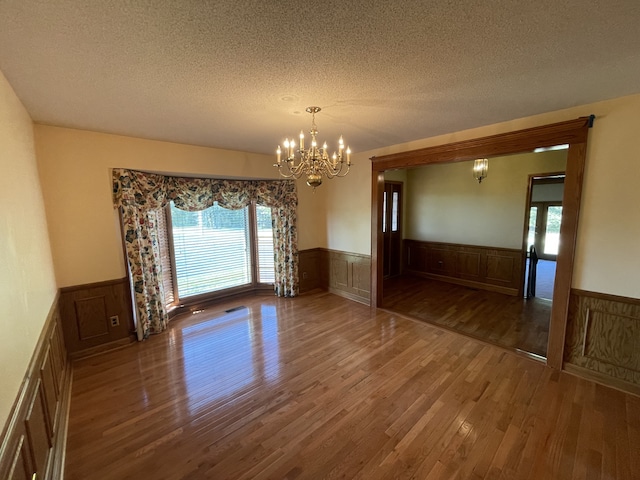 empty room featuring a textured ceiling, wood-type flooring, an inviting chandelier, and plenty of natural light