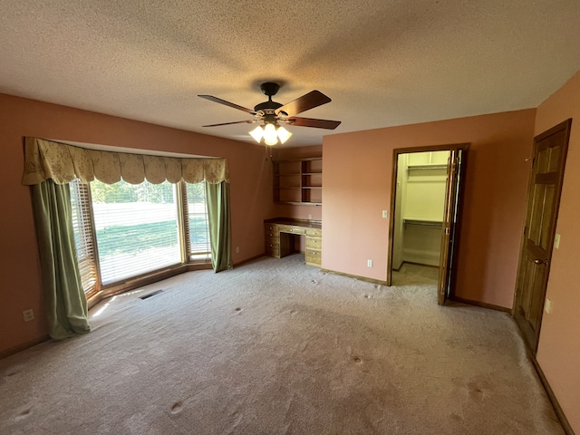 unfurnished living room featuring light colored carpet, a textured ceiling, built in desk, and ceiling fan