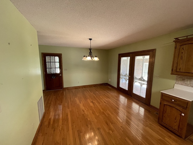 unfurnished dining area with french doors, light hardwood / wood-style floors, a textured ceiling, and a chandelier