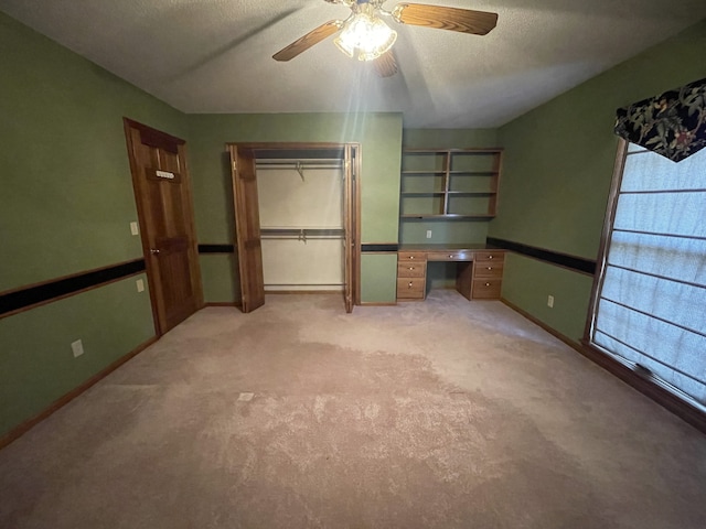 unfurnished bedroom with built in desk, ceiling fan, a closet, and light carpet