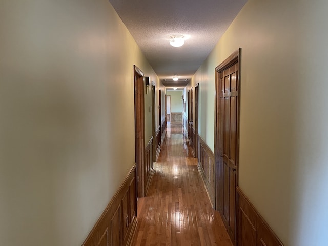 corridor with a textured ceiling and light hardwood / wood-style floors