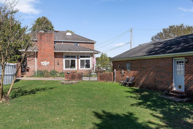 rear view of house featuring a yard, brick siding, fence, and a chimney