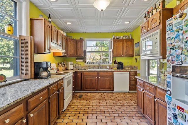 kitchen with brown cabinetry, a sink, an ornate ceiling, under cabinet range hood, and white appliances