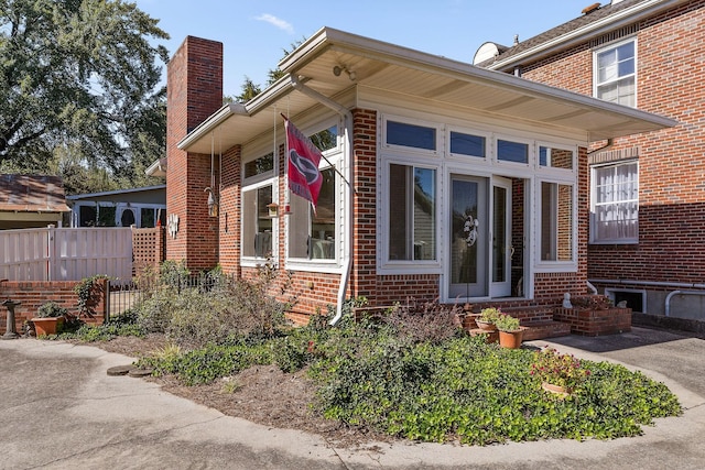 view of side of home with fence, a chimney, entry steps, and brick siding