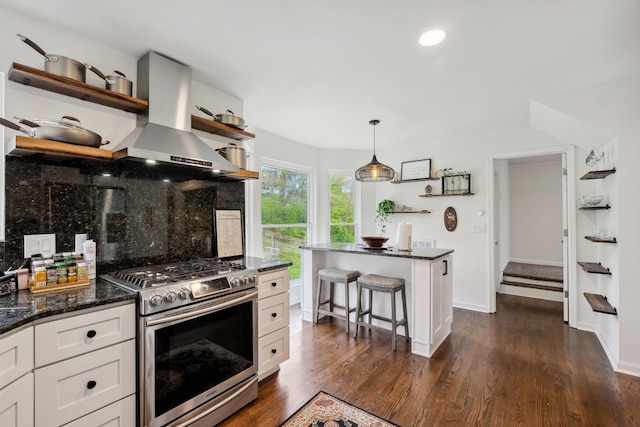 kitchen featuring wall chimney range hood, hanging light fixtures, white cabinetry, stainless steel gas range oven, and dark hardwood / wood-style floors