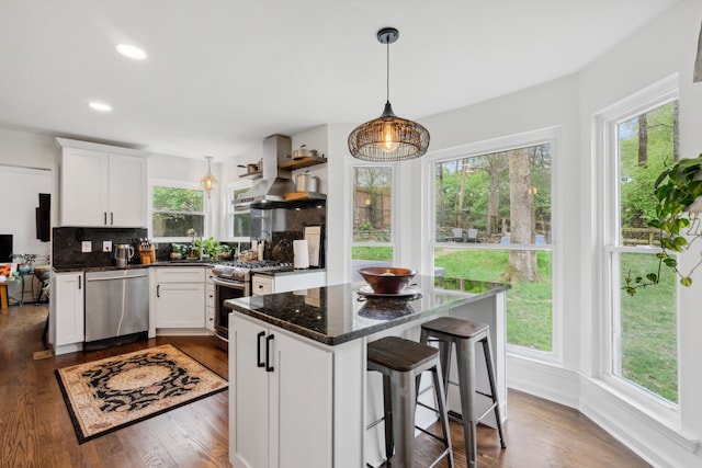 kitchen featuring decorative backsplash, white cabinets, hanging light fixtures, appliances with stainless steel finishes, and dark hardwood / wood-style floors