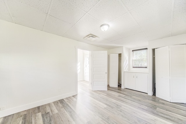 unfurnished room with a drop ceiling and light wood-type flooring