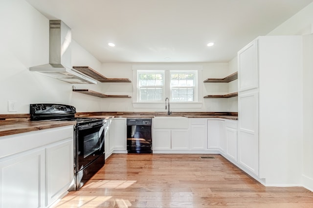 kitchen featuring wall chimney range hood, black appliances, sink, white cabinets, and light hardwood / wood-style flooring