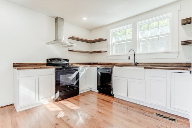 kitchen featuring wall chimney range hood, white cabinets, light wood-type flooring, black appliances, and sink