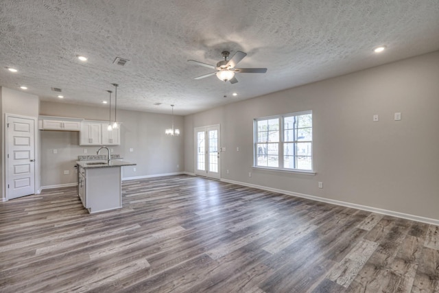 unfurnished living room with ceiling fan with notable chandelier, wood-type flooring, sink, and a textured ceiling